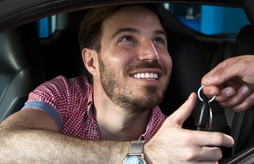 Smiling man in a car receives car keys from another hand.