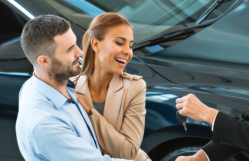 Happy couple smiling as they receive car keys from a salesperson for their new car.